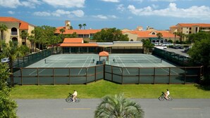 Un court de tennis entouré de bâtiments aux toits recouverts de tuiles rouges et de palmiers.