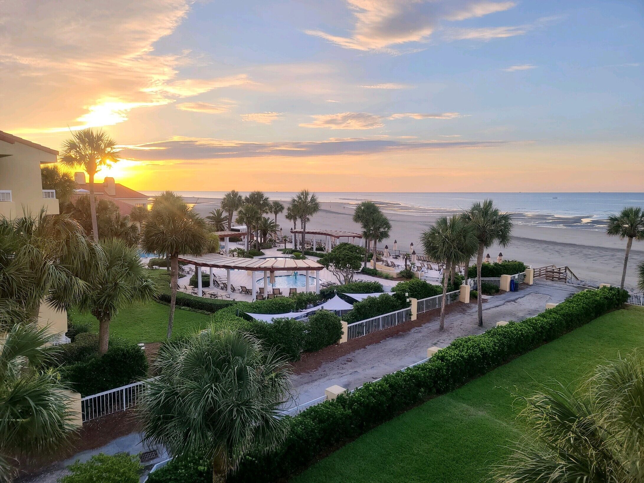 Un resort con piscina, palmeras y vista a la playa al atardecer.