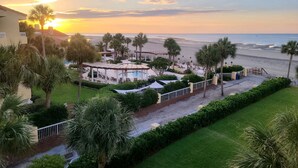 Un complexe hôtelier doté d’une piscine, de palmiers et offrant une vue sur la plage au coucher du soleil.
