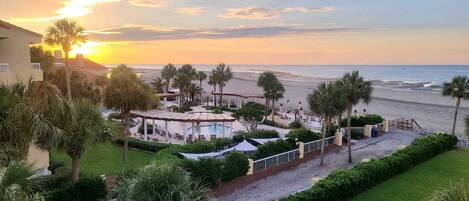 Un resort con piscina, palmeras y vista a la playa al atardecer.