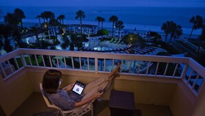 Un balcon avec vue sur la plage, une chaise longue et une personne utilisant une tablette.