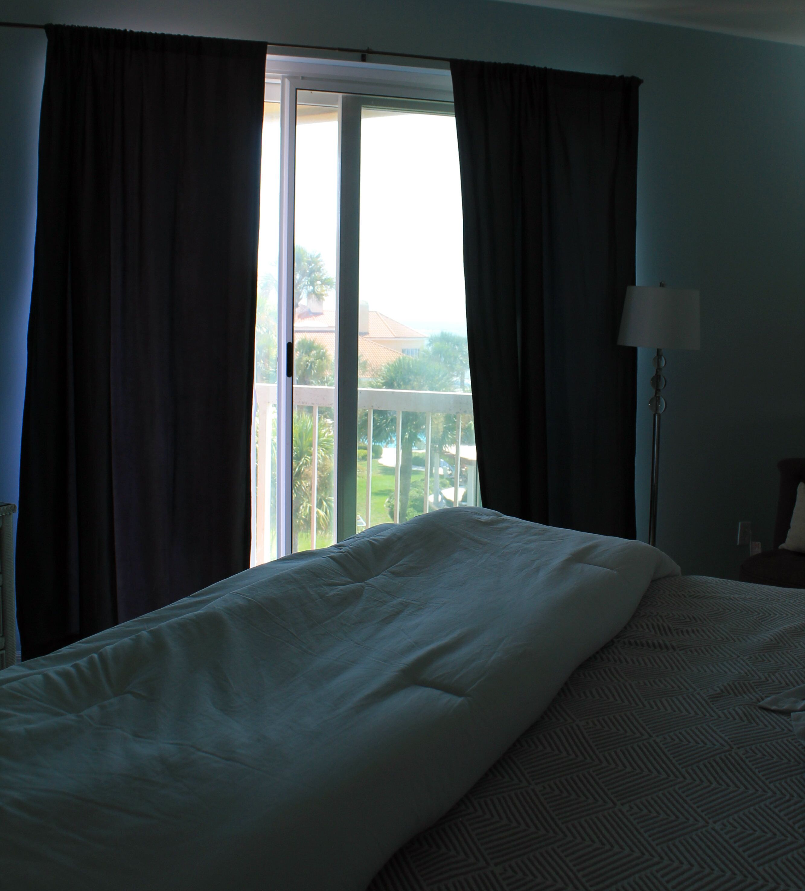 A hotel room with a bed, a view of a balcony, and a lamp.