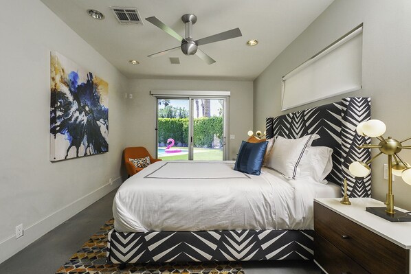 A modern bedroom with a bed, a ceiling fan, a nightstand, and a view of the outdoors.