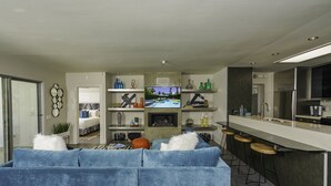Ein modernes Wohnzimmer mit einem blauen Sofa, einem Fernseher und einer Küchenzeile mit einer Bar.