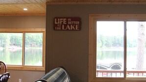 Una habitación con vistas a un lago, techo de madera y un cartel en la pared que dice "La vida es mejor a la orilla del lago".
