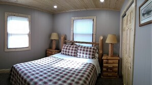 Un dormitorio con una cama, dos mesitas de noche con lámparas, una ventana con persianas y una puerta.