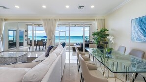 Una sala de estar moderna con una mesa de comedor de vidrio, sofás blancos y vista al océano.