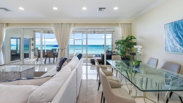 A modern living room with a glass dining table, white sofas, and a view of the ocean.