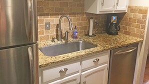 A kitchen with stainless steel appliances, a granite countertop, and a brick backsplash.