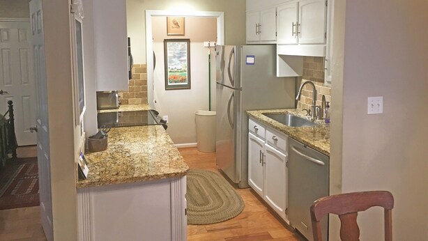 A compact kitchen with granite countertops, white cabinets, a stainless steel refrigerator, and a built-in dishwasher.