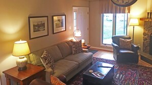A living room with a sofa, armchairs, a coffee table, a clock, and framed pictures on the wall.
