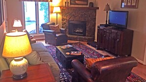 A living room with a fireplace, leather armchair, sofa, and a television on a wooden cabinet.