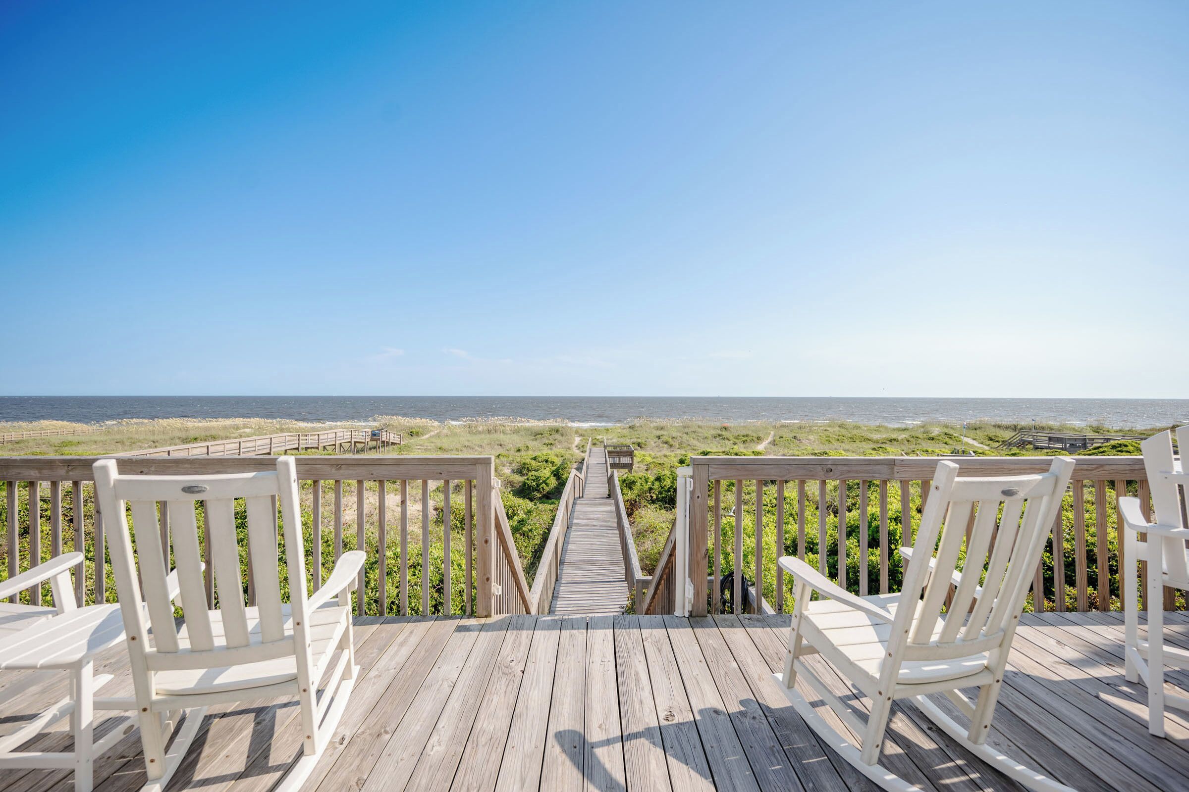 Una terrazza in legno con sedie bianche rivolta verso la spiaggia.