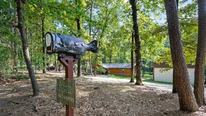 A mailbox with a fish design in a wooded area with a house in the background. - Boomer Bed & Bass; 2 bedroom, 2 bathroom family cabin. (Broken Bow)