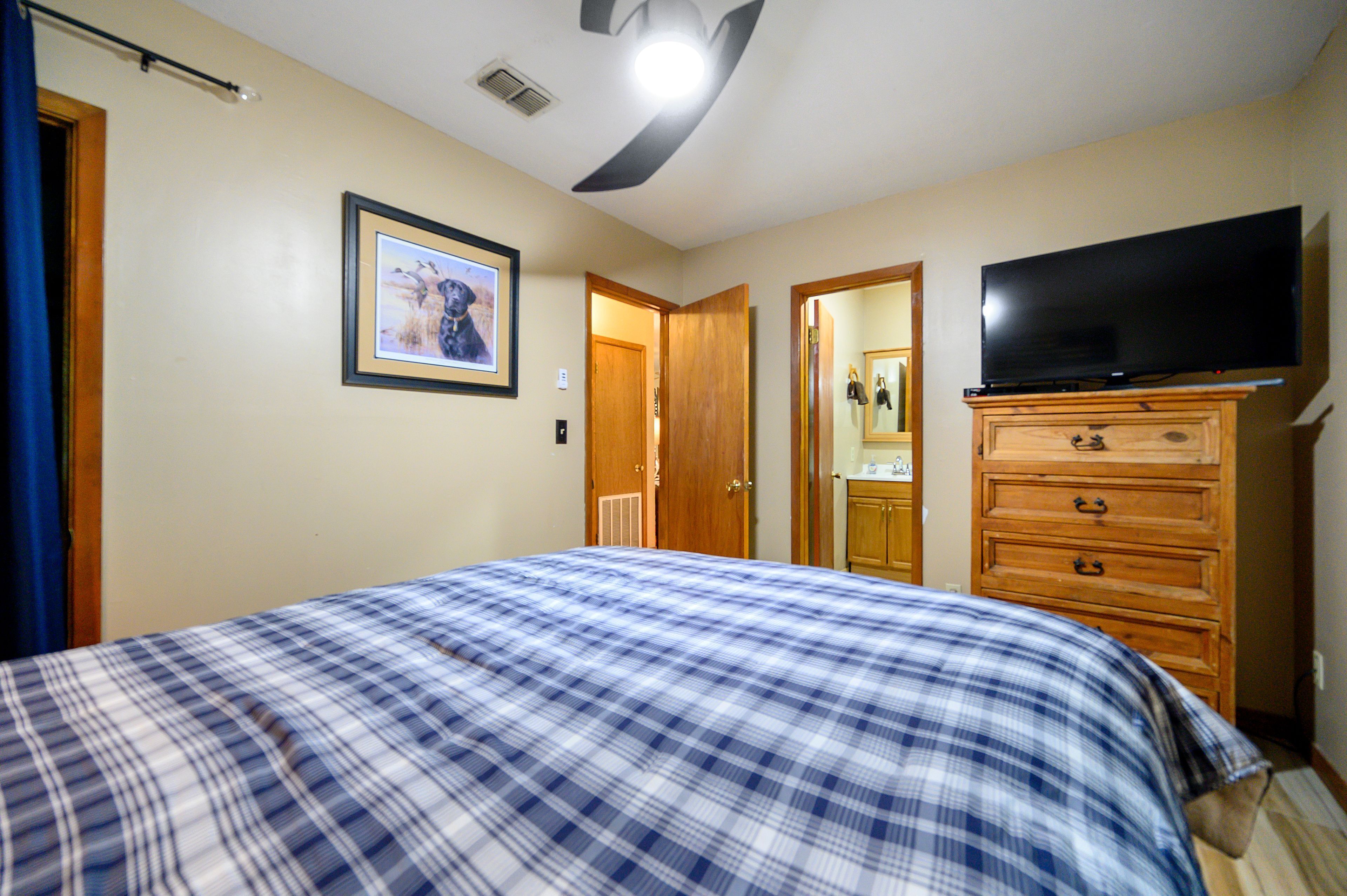 Un dormitorio con cama, cómoda, televisor y un cuadro en la pared.