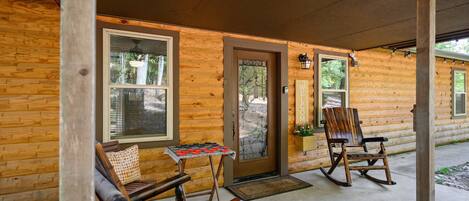 A wooden cabin with a porch, a rocking chair, and a table with a checkered cushion.
