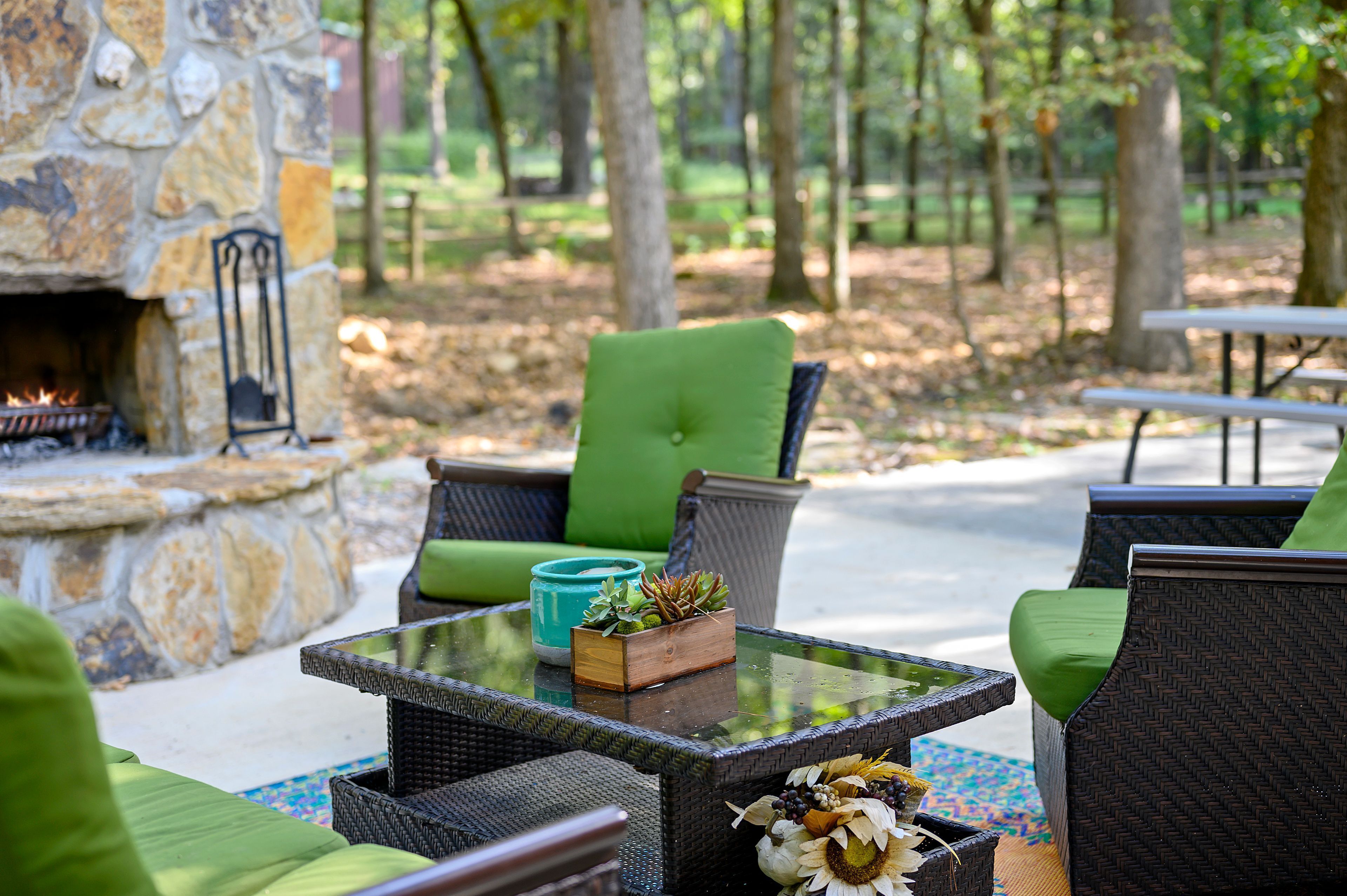 An outdoor seating area with wicker furniture, a stone fireplace, and a glass table.