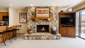 A stone fireplace with a TV above it, a dining area with chairs, and a kitchen with cabinets and a microwave. - Montaneros 217 - 1 Bedroom Platinum (Vail)