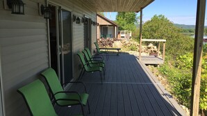 Una terraza techada con sillas verdes, una mesa y vistas a una casa y el paisaje.