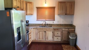 Una cocina con armarios de madera, un refrigerador de acero inoxidable, un lavamanos y una ventana con persianas.