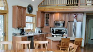 A kitchen with wooden cabinets, a dining table with chairs, a microwave, a refrigerator, and a stove. - "SERENITY 4 ALL SEASONS" (Wintergreen Resort)