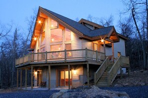 A wooden cabin with a balcony, large windows, and a staircase leading to the main entrance.