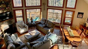 A cozy interior with a stone fireplace, multiple seating areas, and large windows offering a view of the outdoors. - "SERENITY 4 ALL SEASONS" (Wintergreen Resort)