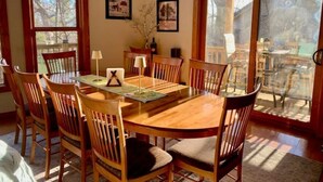 A dining area with a wooden table and chairs, framed pictures on the wall, and a large window with a view of the outdoors. - "SERENITY 4 ALL SEASONS" (Wintergreen Resort)