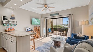 Un salon moderne avec un coin cuisine, un ventilateur de plafond, une télévision et une grande porte-fenêtre coulissante donnant sur une terrasse extérieure.