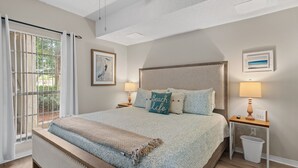 Une chambre avec un grand lit, une table de chevet avec une lampe, un tableau encadré au mur et une vue à travers une porte coulissante.
