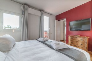A hotel room with a large bed, a TV mounted on the wall, and a view of the city through the window.