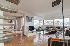 A modern living room with a TV, sofa, and coffee table. There is a staircase with wooden steps and a view of the city through large windows. - Angelo Brunetti 24 - FromHometoRome (Roma)