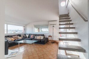 Una sala de estar moderna con un sofá seccional, una mesa de centro de vidrio y una escalera con escalones de madera.