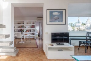 A modern living room with a TV, bookshelf, and dining area.