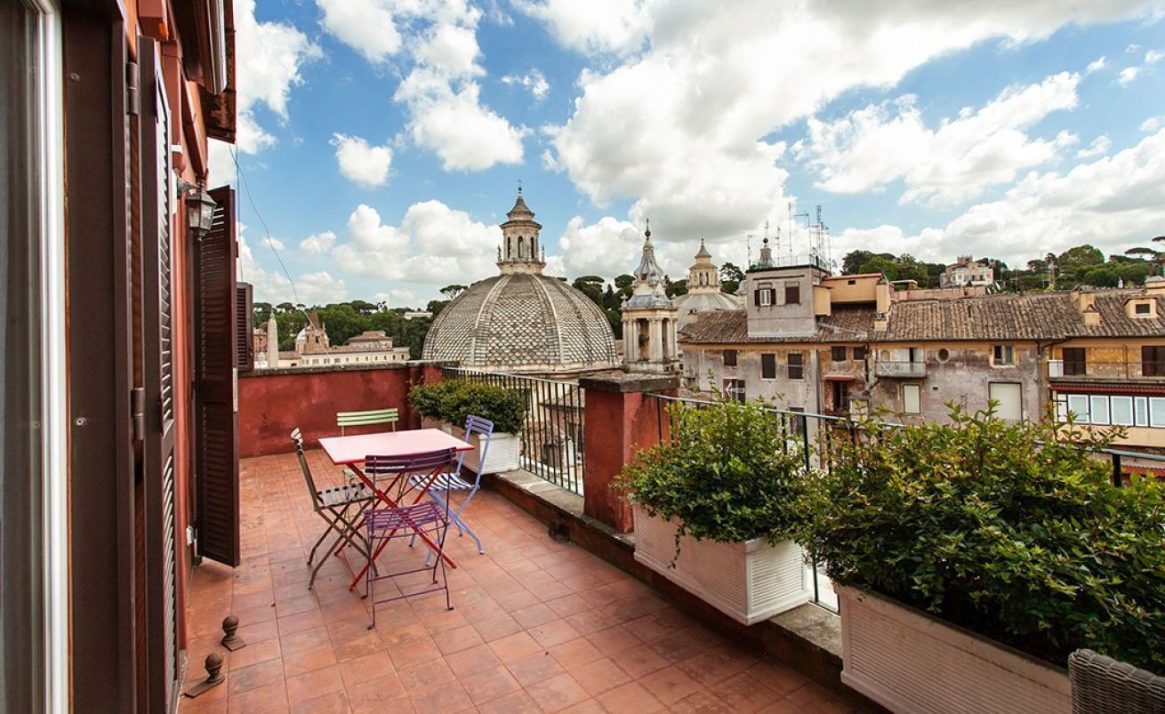 A terrace with a table and chairs, a view of historic buildings, and a clear sky.