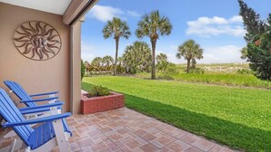 Een terras met blauwe stoelen, een decoratieve zonnewand en uitzicht op een gazon met palmbomen.