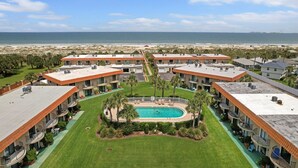 Een resort met meerdere gebouwen, een zwembad in het midden en uitzicht op het strand.
