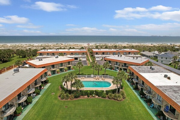 A resort with multiple buildings, a central swimming pool, and a view of the beach.