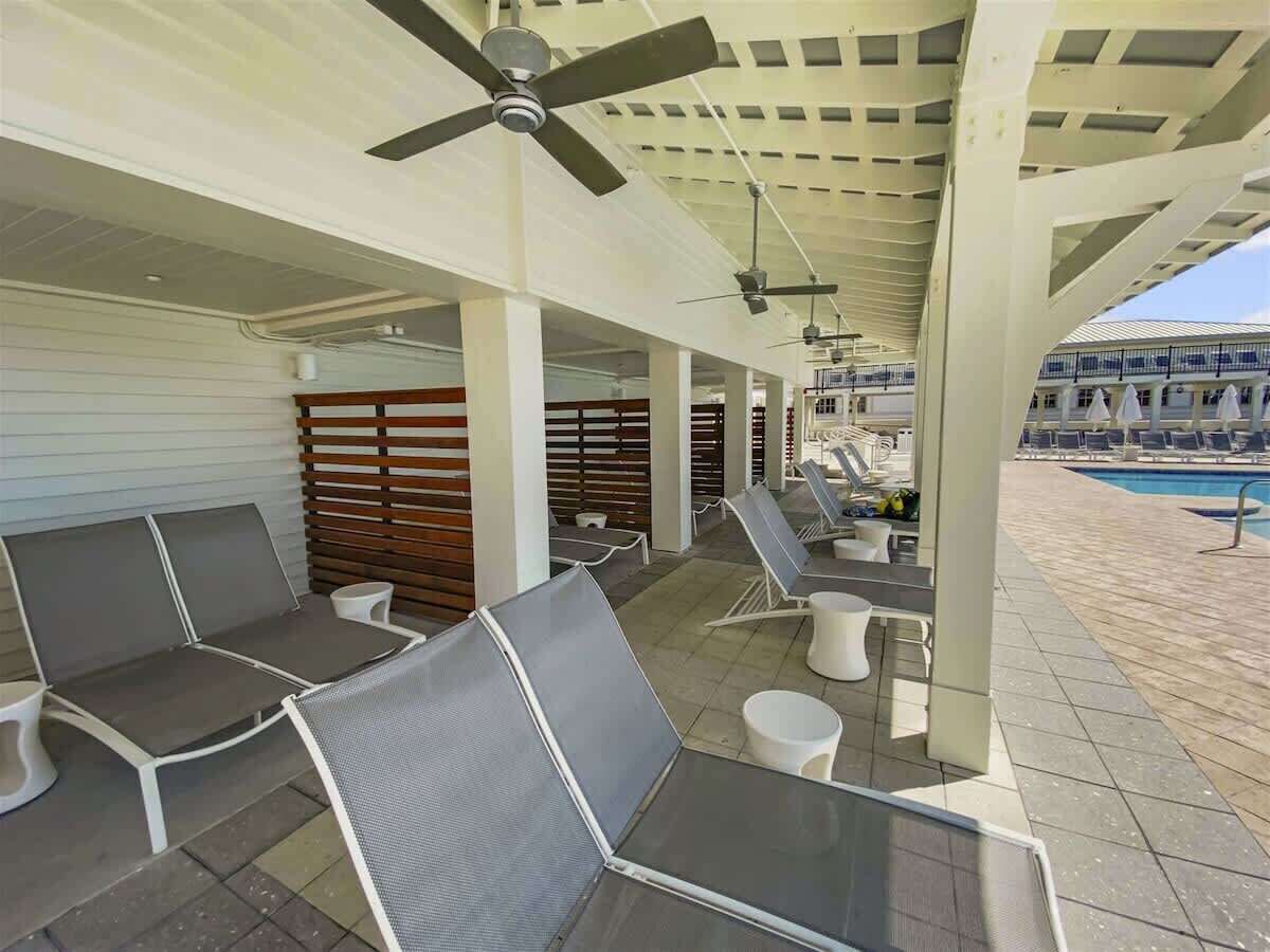 An outdoor seating area with chairs and tables, a ceiling fan, and a pool in the background.
