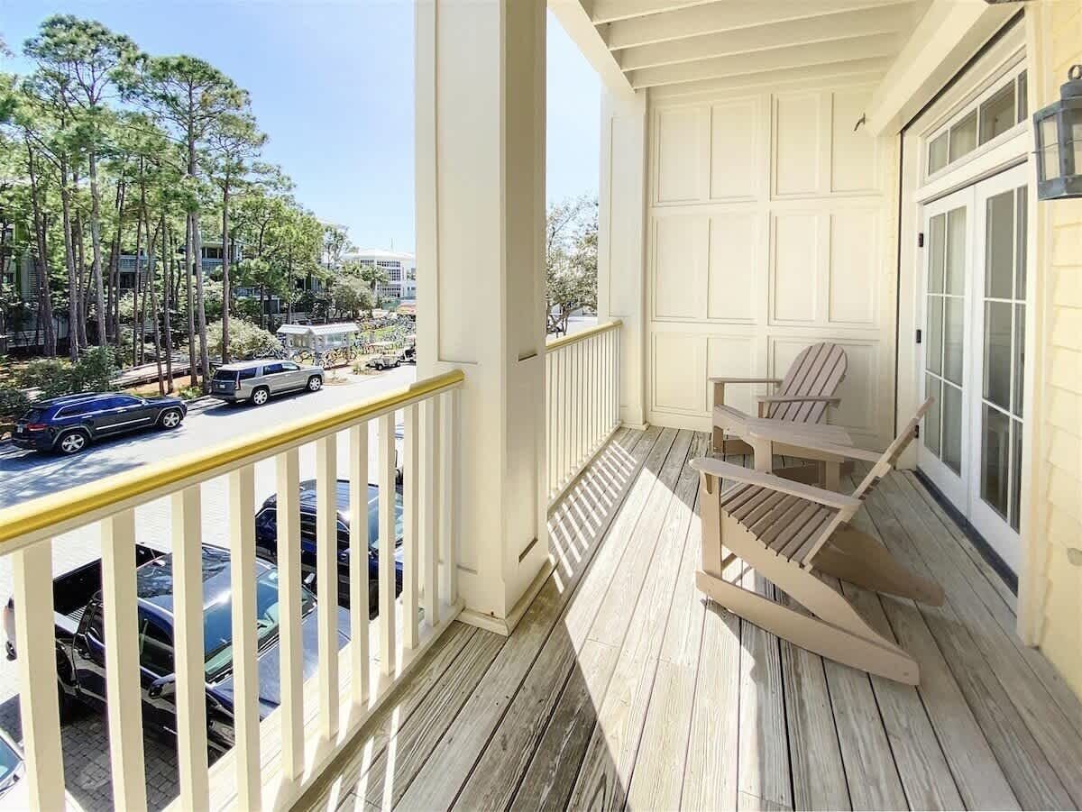A wooden deck with a railing, a chair, and a view of parked cars and trees.