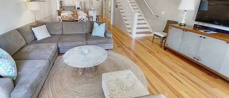 A living room with a sectional sofa, a round coffee table, a rug, a TV, and a staircase.