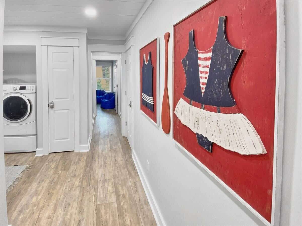 Un pasillo con lavandería, una silla azul y dos obras de arte rojas y blancas.