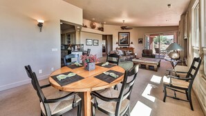 Amplia sala de estar con mesa de comedor, sillas y sofá. Se observa una cocina al fondo, y un patio con mobiliario exterior.