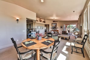 A spacious living area with a dining table, chairs, and a sofa. There is a kitchen in the background, and a patio area with outdoor seating.
