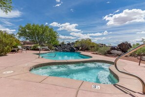 A swimming pool with a hot tub, surrounded by lounge chairs and a rocky landscape.