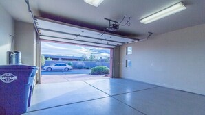Un garaje con un coche estacionado afuera, un contenedor de basura y un proyector instalado en el techo.