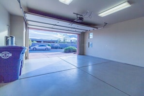A garage with a car parked outside, a trash bin, and a ceiling-mounted projector.