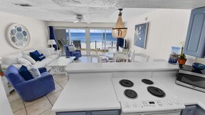 Une cuisine moderne dotée d’un îlot central, de meubles blancs et offrant une vue sur l’océan.
