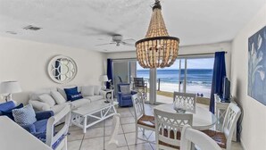 Un espace de vie aménagé au bord de la plage, avec un canapé, des fauteuils, une table et une vue sur l’océan.