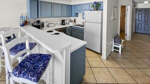 Une cuisine avec des meubles bleus, un réfrigérateur blanc et un coin bar doté de tabourets bleus avec des coussins.